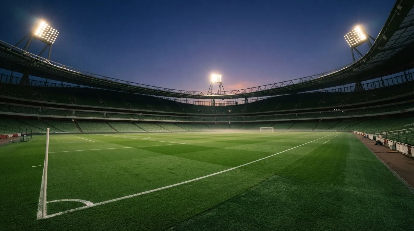 An empty football stadium with floodlight masts at dusk