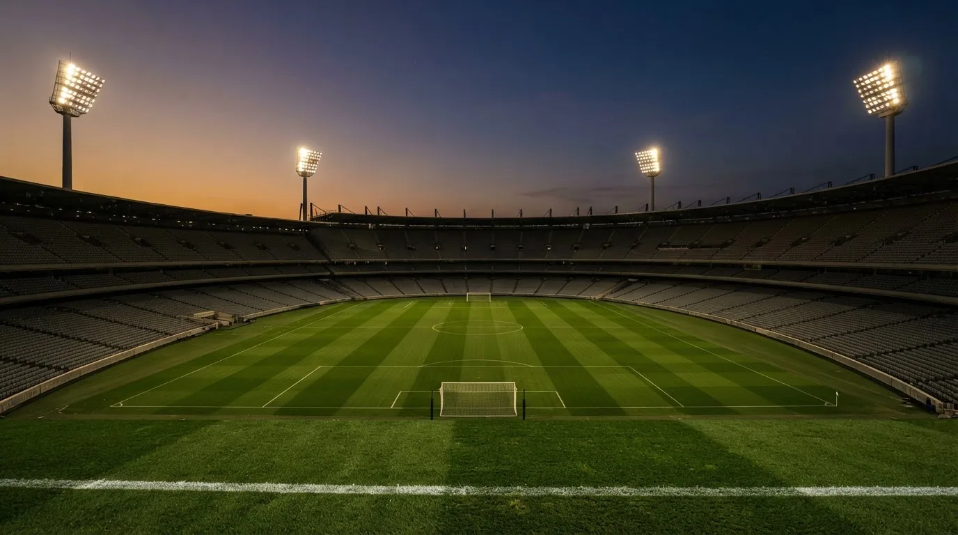 An empty football stadium with floodlight masts at dusk