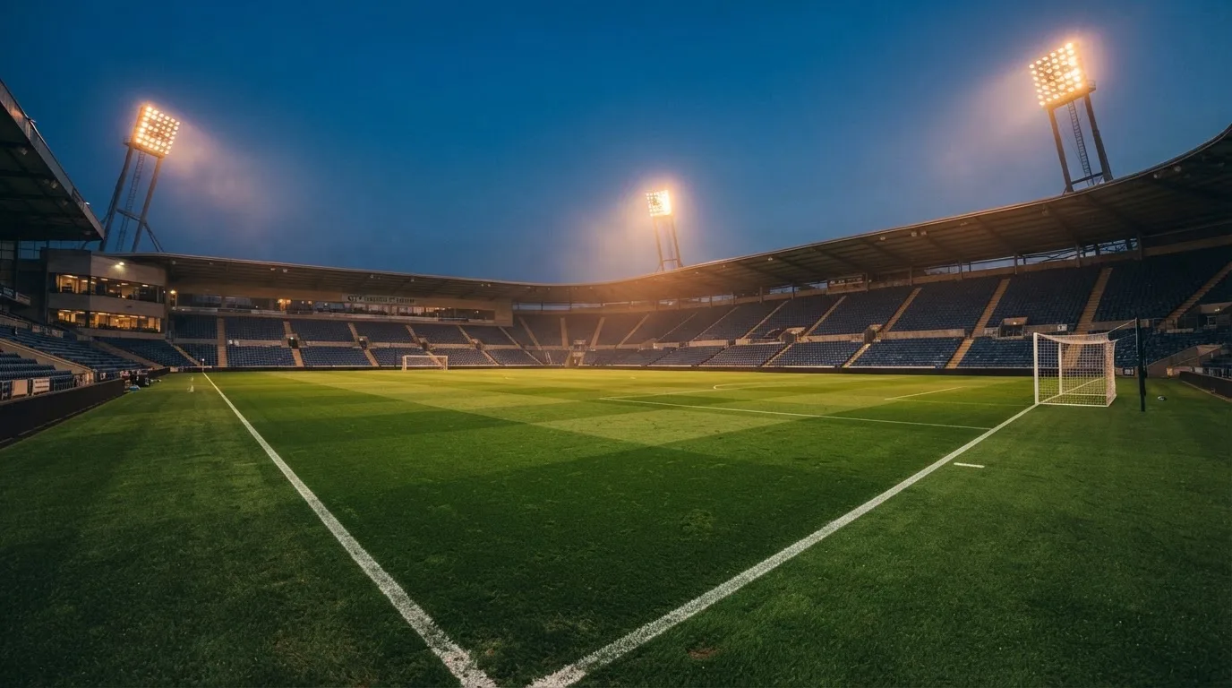 An empty football stadium with floodlight masts at dusk