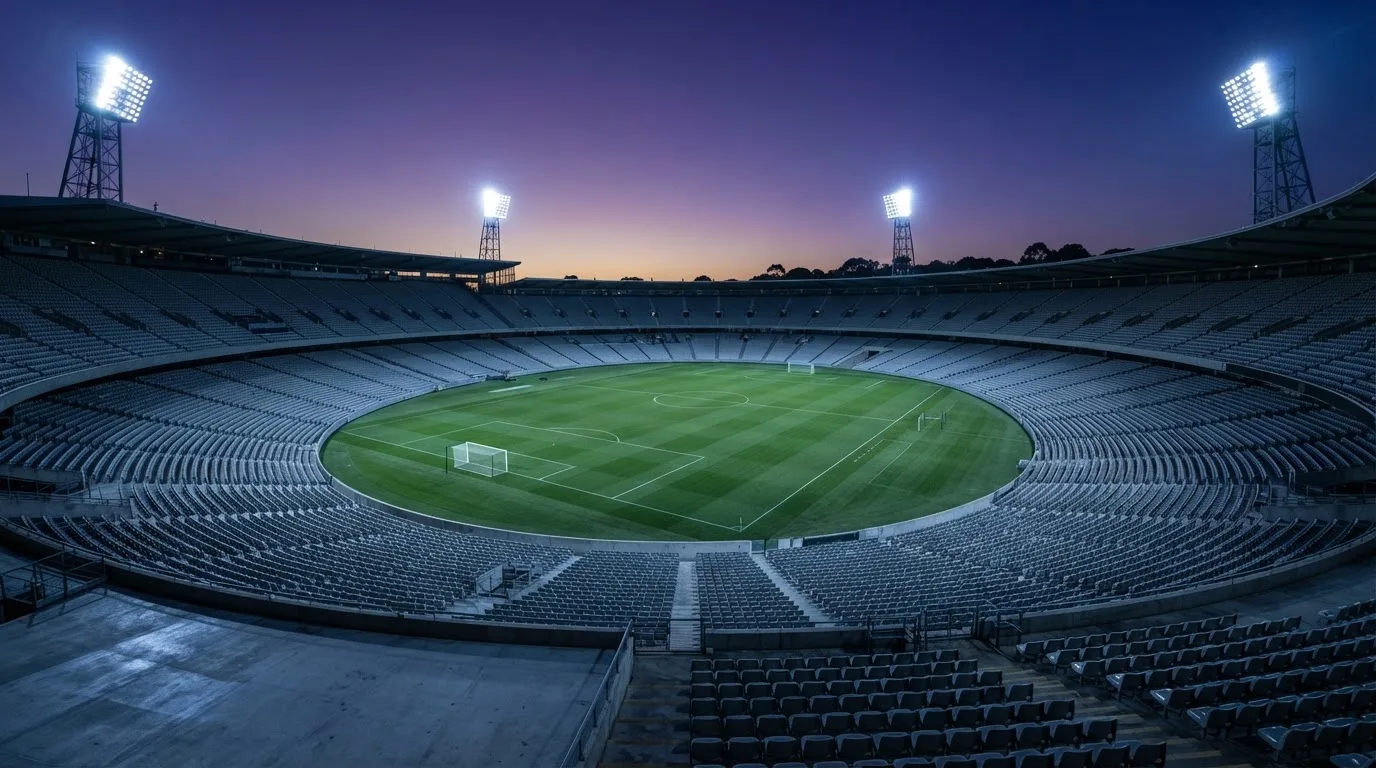 An empty football stadium with floodlight masts at dusk