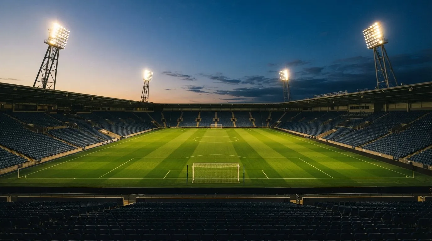 An empty football stadium with floodlight masts at dusk