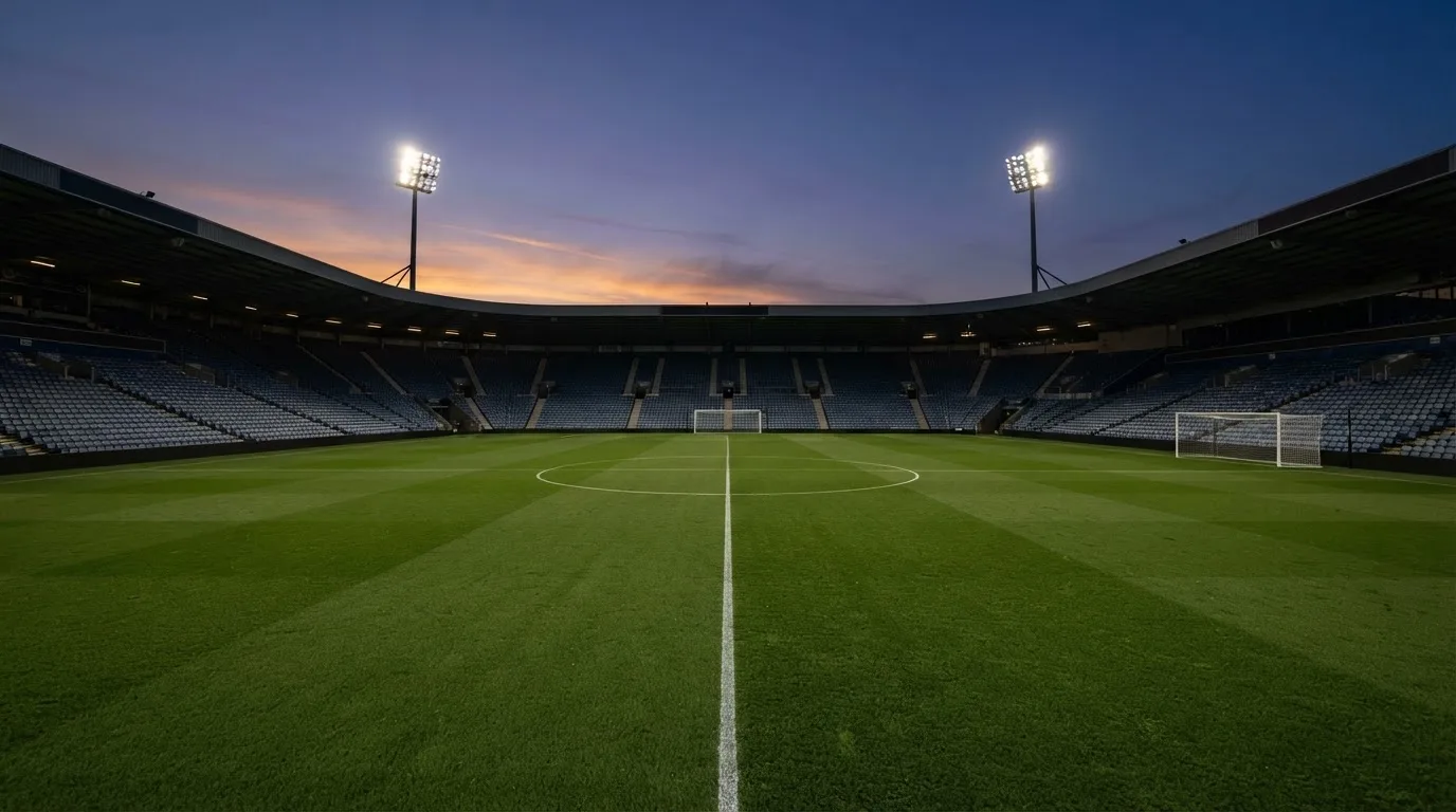An empty football stadium with floodlight masts at dusk