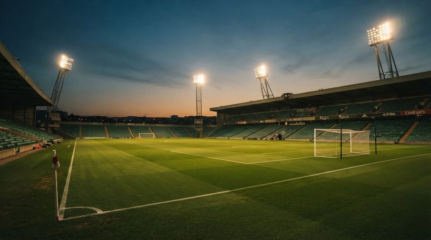 An empty football stadium with floodlight masts at dusk