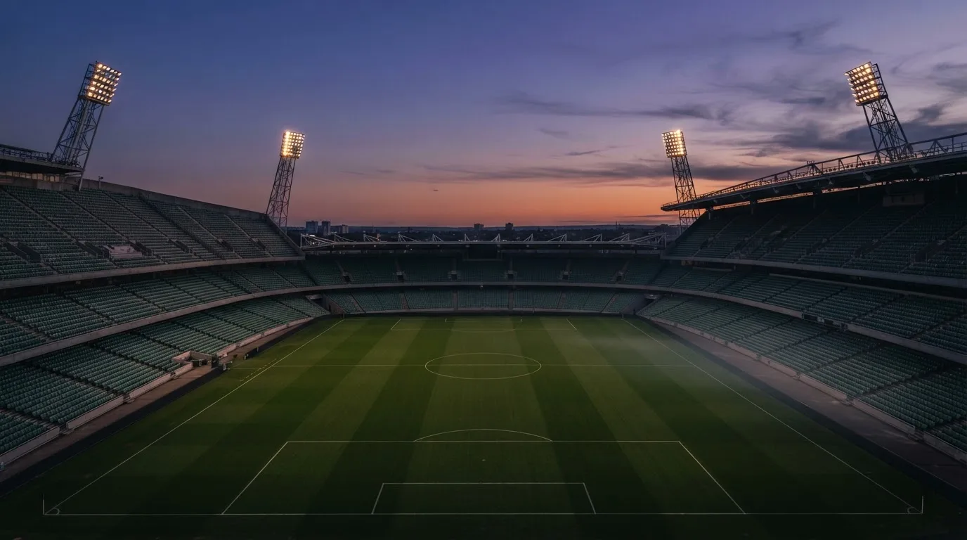 An empty football stadium with floodlight masts at dusk