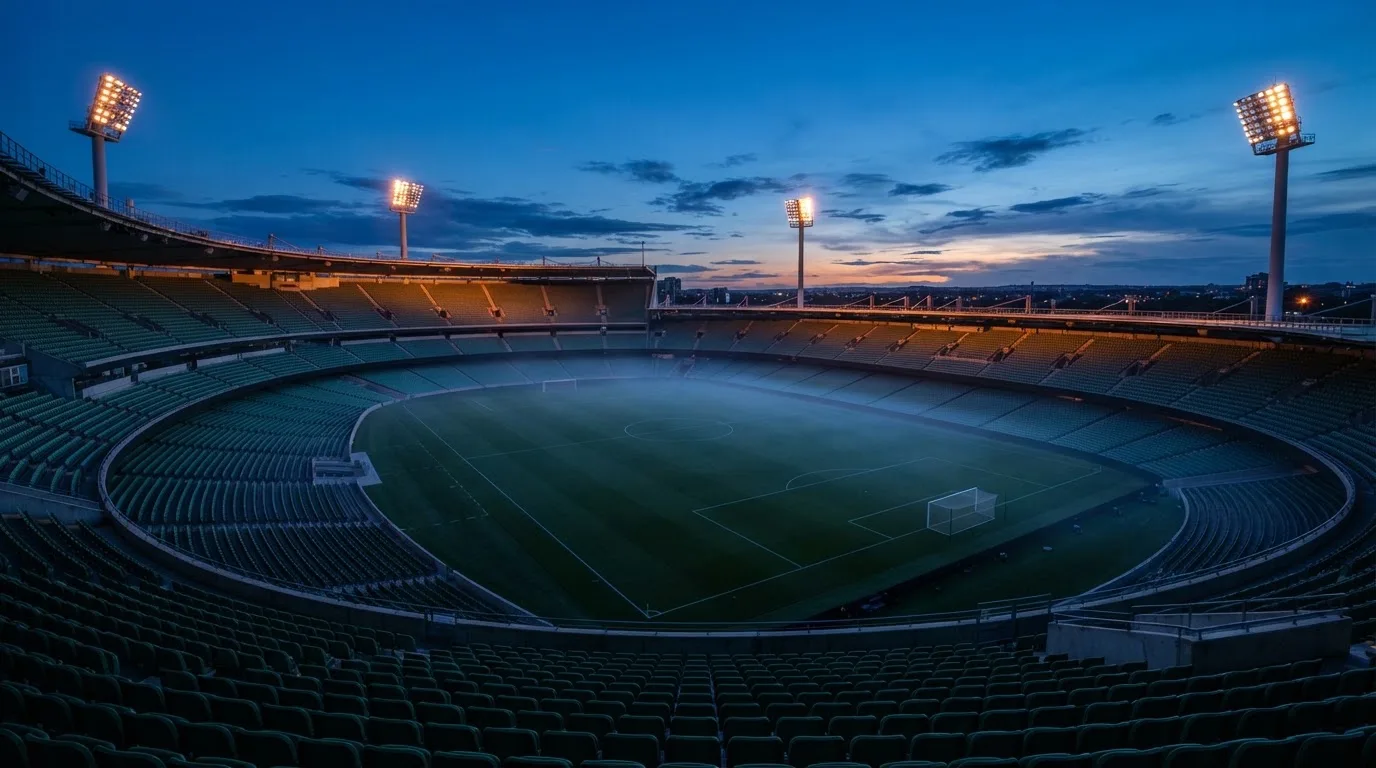 An empty football stadium with floodlight masts at dusk