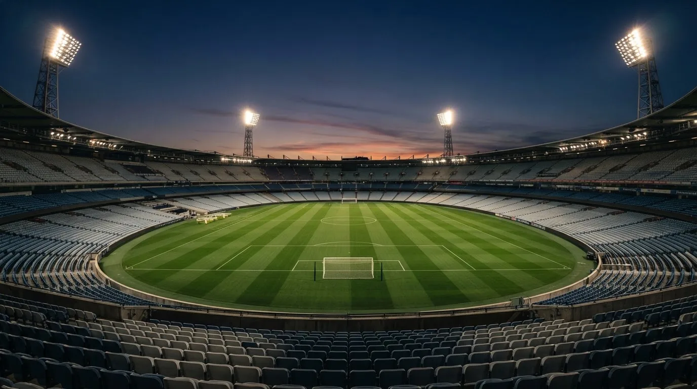 An empty football stadium with floodlight masts at dusk