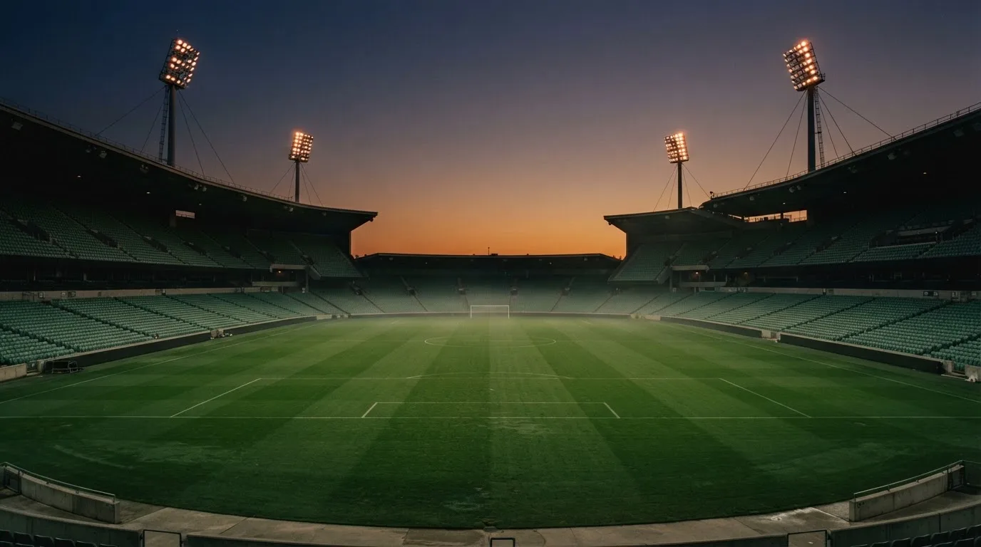 An empty football stadium with floodlight masts at dusk