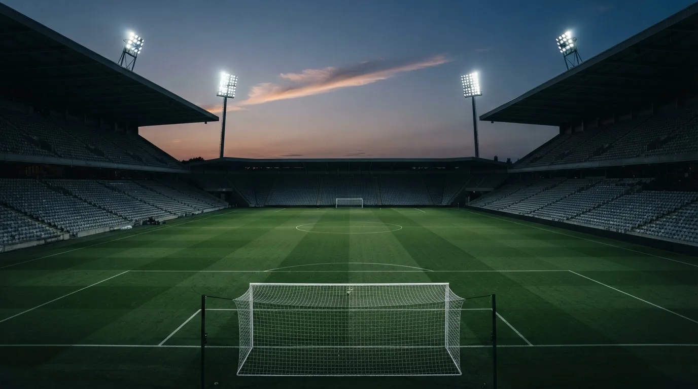 An empty football stadium with floodlight masts at dusk